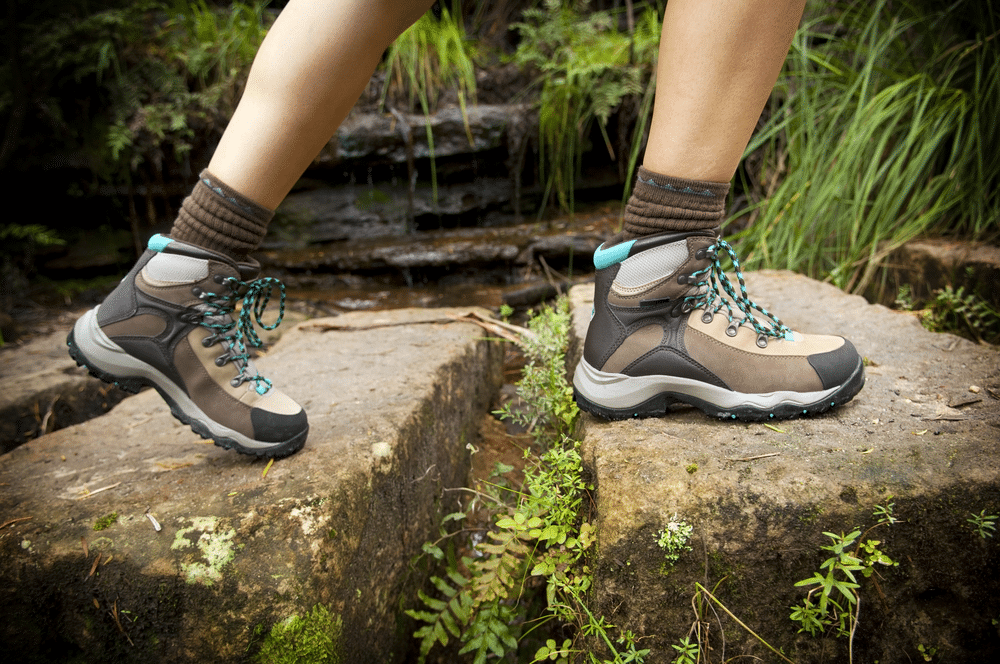 A side view of a woman stepping on stones wearing hiking shoes