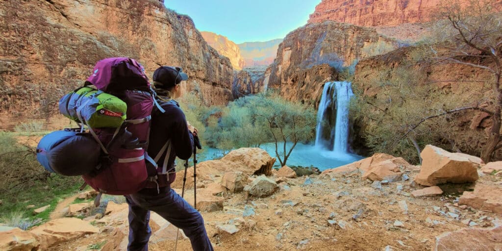 a female hiker with a fully packed backpack standing in front of waterfall