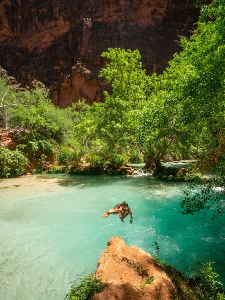 a hiker jumping into water in havasu fall