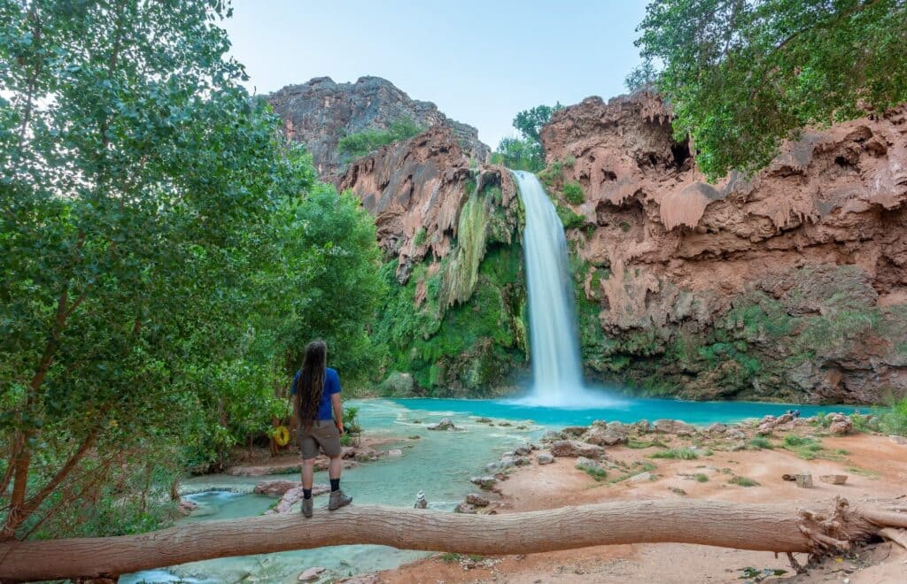 a hiker standing on a wooden log infront of waterfall