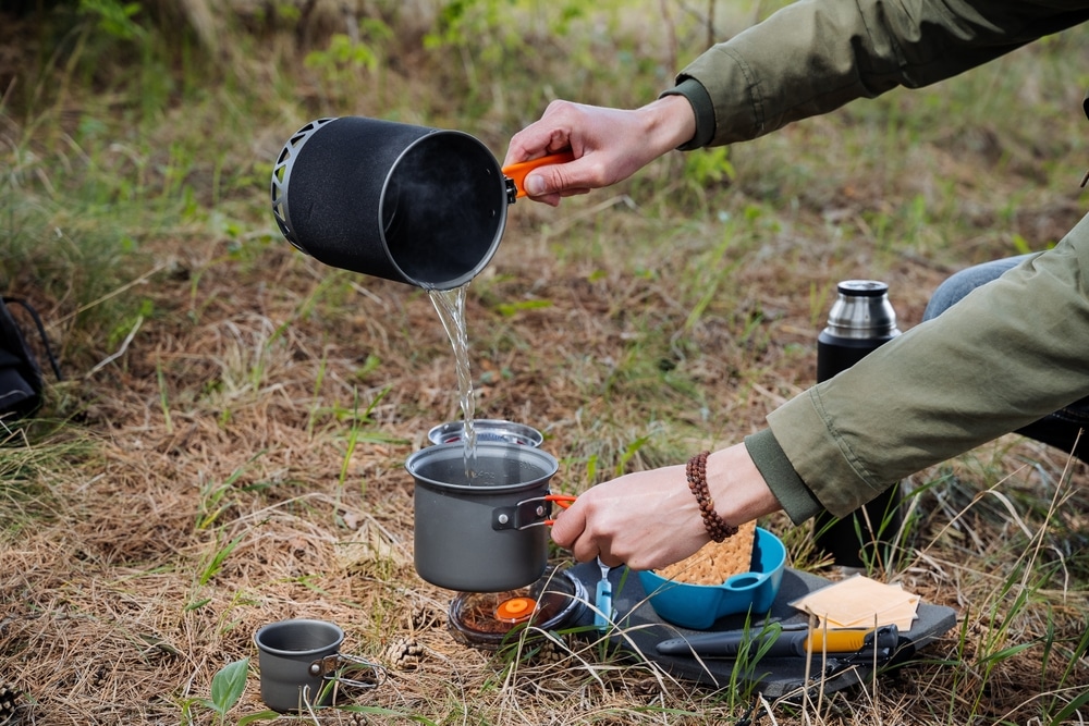 A tourist pours hot water from a pot into a pot, cooks food in the camp