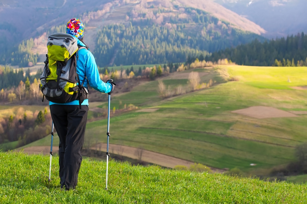  Beautiful young woman hiking happy with Trekking pole stands on a meadow