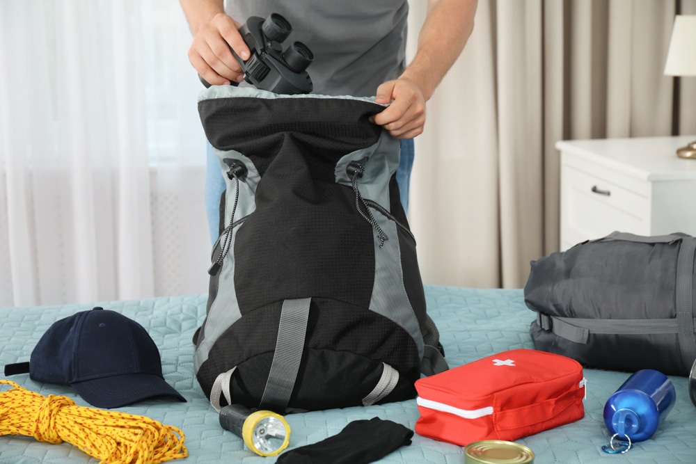 Man packing different hiking equipment into backpack at home