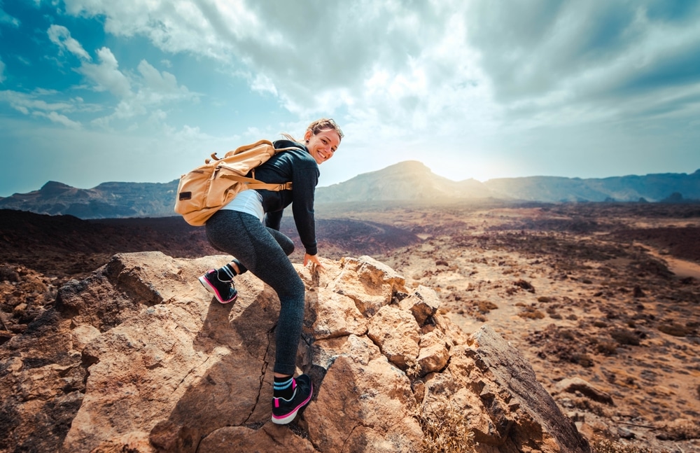 Portrait of a happy woman hiker standing on the top of mountain ridge against mountains