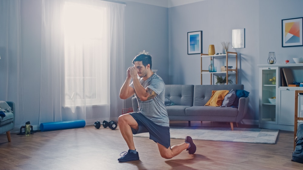 Strong Athletic Fit Man in T shirt and Shorts is Doing Forward Lunge Exercises at Home