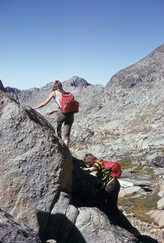 Two female hikers are scrambling over rocks on a hiking trail