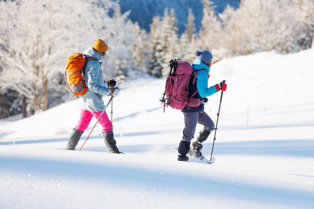 Two women walking in snowshoes in the snow holding hiking poles