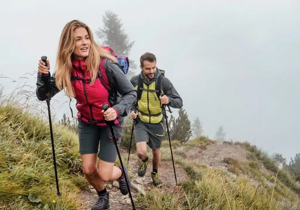 a male and female hiker walking through a path holding the poles