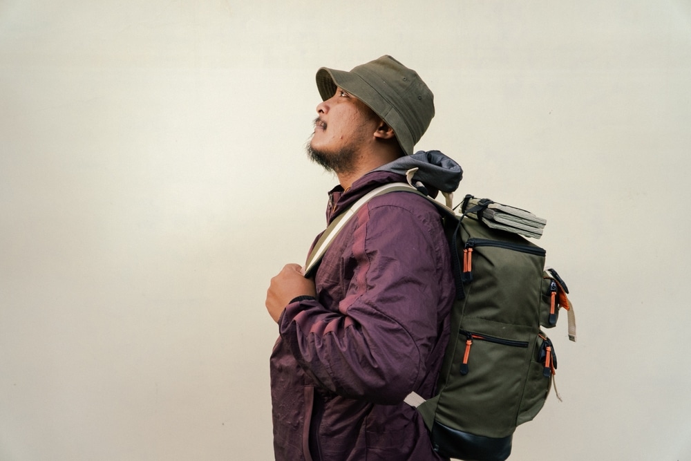 Half body portrait of adult man wearing hiking outfit with jacket, bucket hat, carrier bag