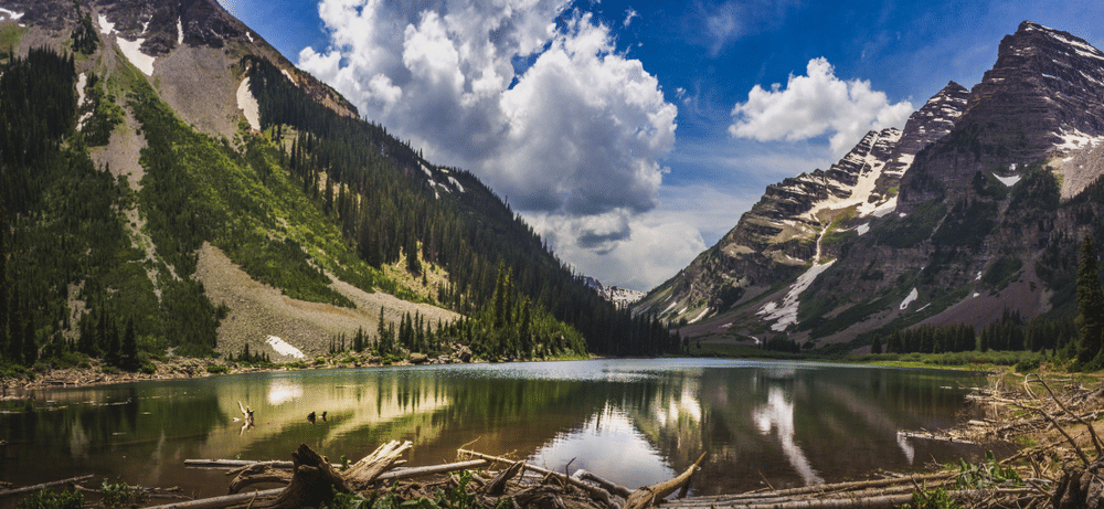 Panorama of Pyramid Peak (left), Maroon Bells (right), and Crater Lake in Snowmass Wilderness in Aspen, Colorado with a blue sky and clouds in summer